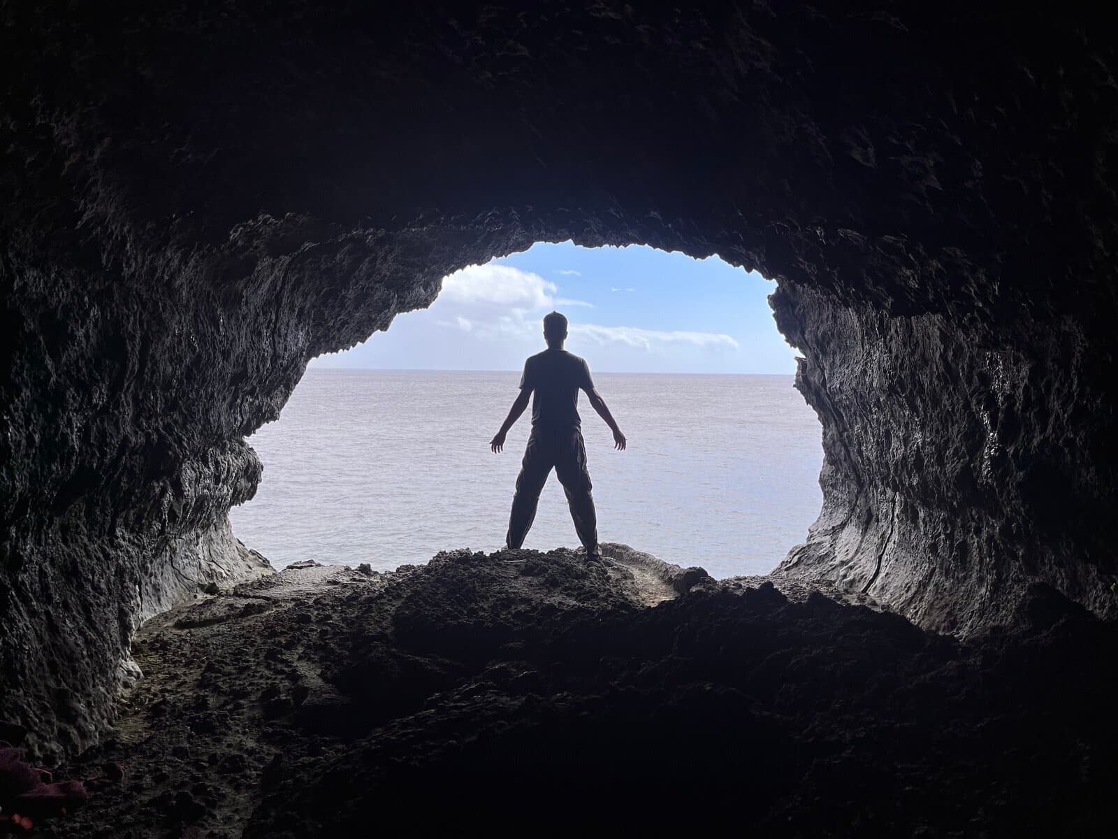 Solo figure standing in the mouth of a lava sea cave, framed by the natural arch, ocean beyond