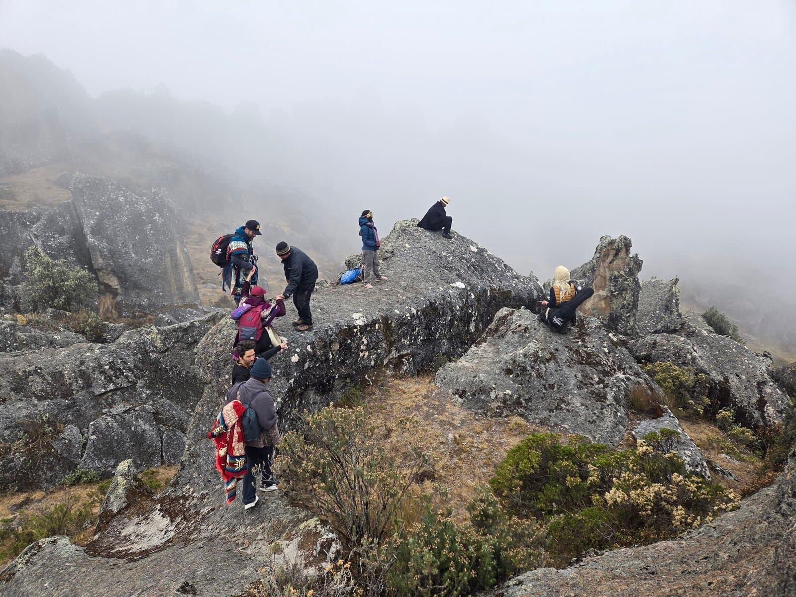 Pilgrim group navigating a misty rocky outcrop in the high Andes