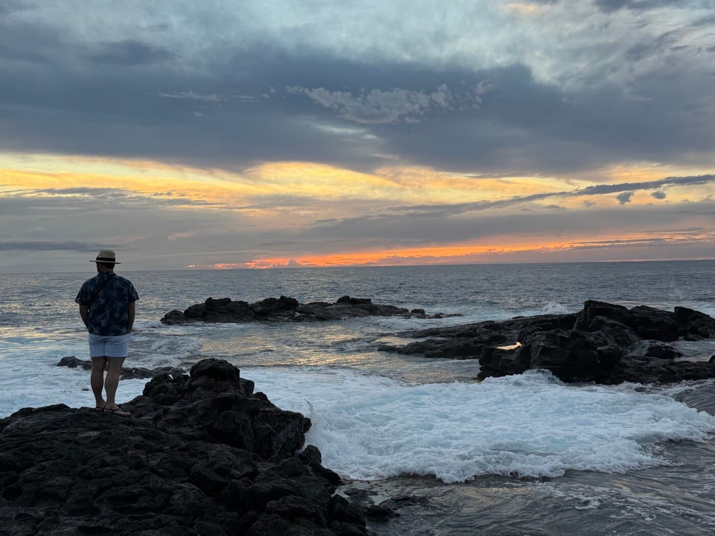 Lone figure looking out at a Big Island sunset over rocky volcanic coastline