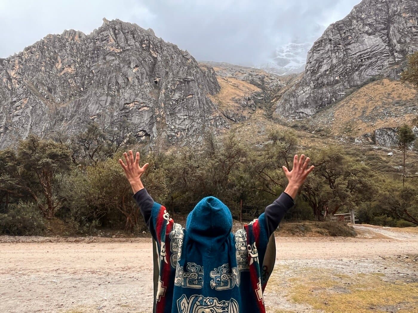 Pilgrim in poncho with arms raised toward Andean peaks