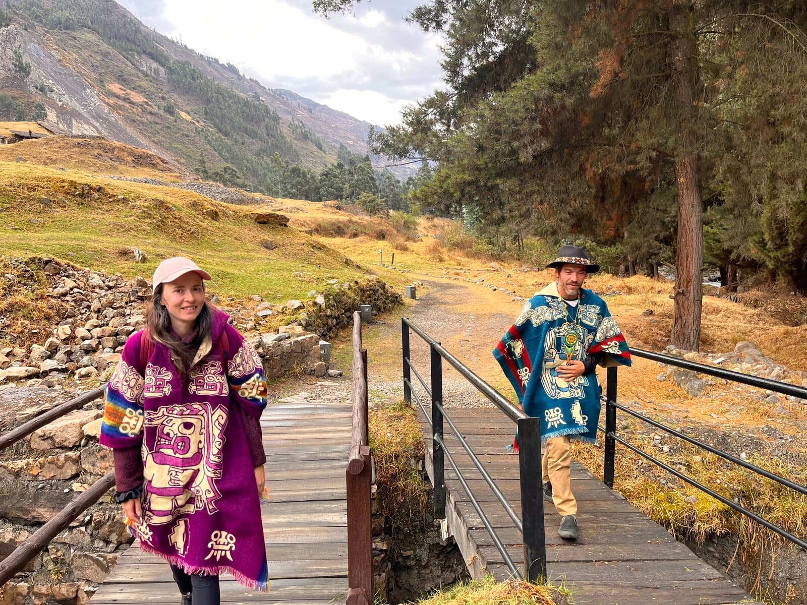 Two pilgrims in colorful Andean ponchos on a bridge in the mountains